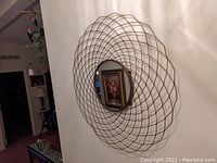 View of the wire spirograph style mirrored wall art mounted on the wall, showing the full piece and some surrounding room details.