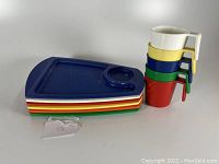 Stack of 6 colorful plastic trays with 5 stacked matching plastic cups on side, showing shape and color contrast