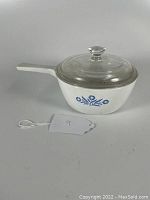 Front view of 1.5 pint white Corning Ware Blue Cornflower saucepan with glass lid and white handle.