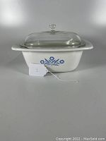 Square white CorningWare Dutch oven featuring the Blue Cornflower pattern on front side with clear glass lid topped with a square knob.