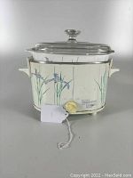 Front angled view of Rival Crock-Pot with Corning Ware Shadow Iris floral pattern on white body, clear glass lid and beige knob