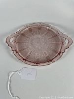 Top-down view of the round pink Depression glass tray with two handles and Cherry Blossom pattern showing scalloped edges and floral impressions.