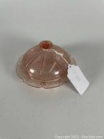 Pink Depression glass dome cover with raised cherry blossom pattern and round knob handle on the top.