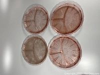 Top-down view of 4 pink depression glass plates with distinct three-section divisions and Cherry Blossom pattern, arranged side by side.