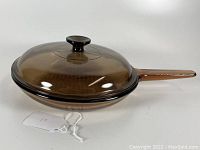 Brown transparent glass skillet with matching lid and integrated handle and lid knob, shown from a slight angle.