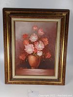 Full view of framed floral oil painting showing bouquet in peach-colored vase, artist signature visible.