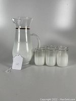 White Blendo glass pitcher with six matching tumblers, all featuring gold trim, shown on a plain white background.