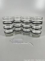 Front view of set of four clear glass tumblers with black and white ring stripes, arranged in a row.