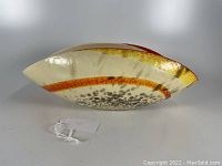 Side profile of the warped art glass bowl showing the speckled and yellow color pattern around the base with a cream-colored exterior.