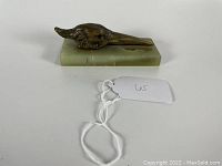 Side view of brass bird head mounted on a green marble rectangular base showing the profile of the bird head with detailed feathers and beak.