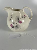 Photo of cream-colored porcelain ball pitcher with pink and black hand-painted thistle floral design, showing full front and left side with curved handle and spout