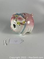 Side view of vintage pink ceramic piggy bank with floral decoration and coin slot on top.