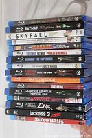 Blu-ray discs stacked showing spine titles for 16 movies including Constantine City of Demons, Batman, Skyfall 007, Iron Man, Suicide Squad, Justice League, Jackass 3, and more.