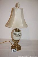Full view of the Lenox table lamp showing brass base, porcelain body with cut-out design, original fabric shade and decorative finial on top.