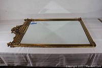 Full view of the antique gilded mirror lying flat on a table, showing the ornate gilded frame with a decorative crest and fluted sides.