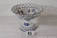Front view of the blue and white reticulated ceramic footed compote bowl showing scalloped rim, cut-out pattern and pedestal base with floral decorations.
