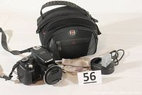 Camera body, lens capped, carrying case, charger with battery inserted, cleaning cloth on white background