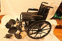 Full side view of black folding wheelchair showing frame, upholstery, leg rests, and wheels.