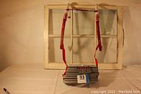 Photo of the folded metal ladder with red hooks and silver steps, showing ladder hanging on old window frame, facing front.
