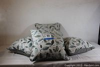 Four square throw pillows with a leaf pattern in greens and grays on light fabric shown arranged together with one facing forward to show pattern.