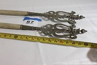 Close-up photo showing metal decorative tops with intricate scroll design and ring detail with measuring tape showing length approximately 7 feet.