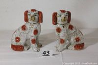 Pair of cream-colored ceramic spaniel dogs with brown spots, painted chains and lockets around neck. Both dogs seated.