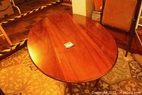 View of the top of the oval wooden table showing the smooth finish, oval shape, and drop leaves in open position with the measuring card on top.