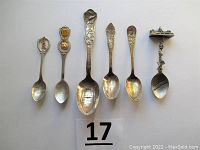 Six souvenir spoons laid out flat and photographed from above to show full spoons in the lot