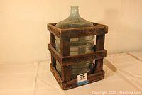 Full view of 5-gallon glass water bottle inside original wooden crate showing structure and bottle neck.