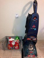 Full view of the Bissell Pro Heat 2X carpet shampooer upright unit and basket containing cleaning solution bottles