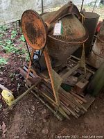 Front side view of the cement mixer showing the large rusted metal drum, hand crank wheel, and metal frame base with one tire visible.