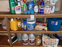 Shelf with assorted cleaning products including dish soaps, cleaners, trash bags, ammonia containers, rice bags, and twine spool.