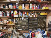 Shelf with multiple paint cans, small containers, and two multi-drawer cabinets containing numerous nails, bolts, and hardware pieces