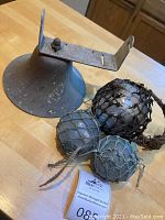 All items in the lot displayed on wooden table including the three glass floats and large metal bell with bracket