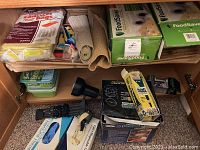 View showing FoodSaver bags and rolls, rubber gloves, Swiffer refills, rolled mats or towels, and a black lamp part inside cabinet.