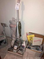 Full view of Kirby Generation 3 upright vacuum cleaner with attached vacuum bag, power cord wrapped on handle, and cleaning shampoo bottle on floor next to it