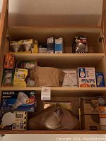 Full cabinet shelf showing neatly arranged lightbulb boxes and some loose bulbs, multiple brands including Philips and GE.
