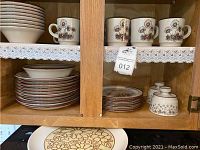 Photo showing entire set of plates, bowls, cups, and sugar bowls neatly arranged in a cabinet.
