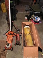 Photo showing two orange hydraulic floor jacks and a yellow portable heater in a box on a concrete floor.