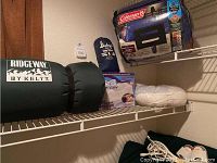 Wide photo showing all items on a wire shelf including the sleeping mat, two Coleman sleeping bags, a camp pillow, leg pillow, and heated blanket.
