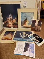 Overview of all photographs and prints arranged on floor showing various rockets and space shuttle images