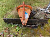 Front view of orange triangular mounting frame with attached steel blade on grass