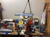 Full view of the workbench surface crowded with various tools including orange and black Chicago chainsaw sharpener, extension cable, boxed items and measuring tools.