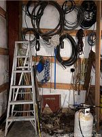 Full view of the lot showing weed torch on wheels, ladder, hoses, various ropes, pulleys, and hardware items hung on walls or placed on floor
