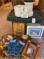 Whisper Mill grain mill, owner's manual, 28-gallon tote, picture frames, chocolate molds, and fall-themed tablecloth visible on floor and tote.