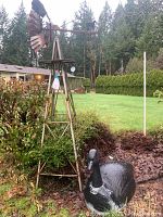Metal garden windmill standing next to a plastic goose outdoors in a garden setting.