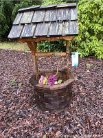 Full view of the wooden wishing well showing the roof, well basin, and handle with artificial flowers inside.