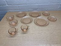 View of full set displaying 4 dinner plates, 4 smaller plates, 2 cups, and 2 bowls all made of pink glass with swirl patterns.