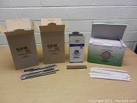 Boxed and loose drinking straws including white individually wrapped paper straws and black unwrapped straws, displayed on a table against a light brick wall