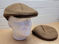 Brown men's cab hats, medium size, one on mannequin head and one laid flat